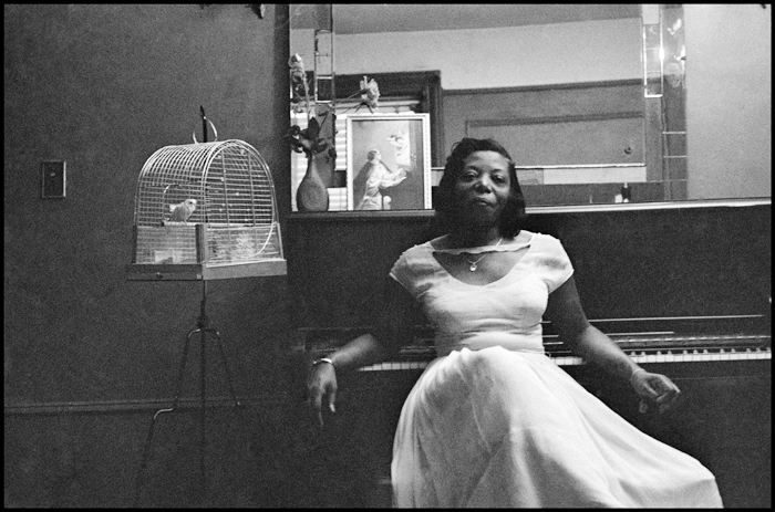 Mary Lou Williams resting against the piano in her Harlem apartment in 1958. The framed image on the piano is Saint Cecilia, patron of musicians. Photo © Dennis Stock/ Magnum Photos, Inc.